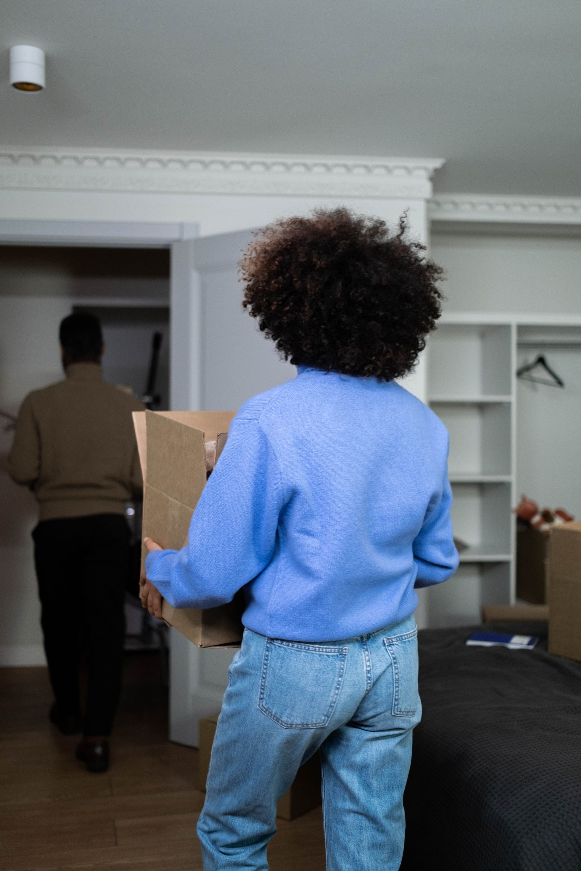 Rear view of woman carrying box in home during move-in day, emphasizing moving and relocation theme.